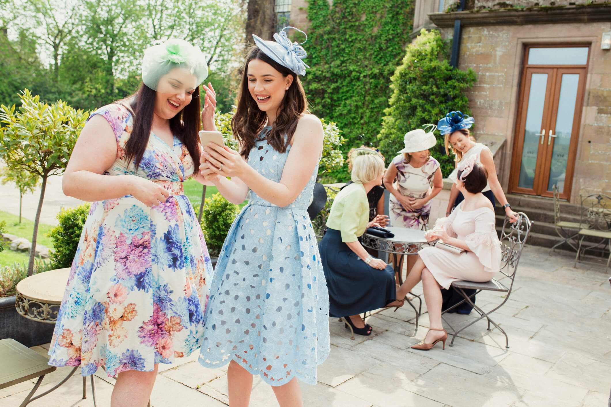 A group of elegant ladies in exquisite dresses and fascinators gracefully posing outdoors, exuding timeless beauty and sophistication.